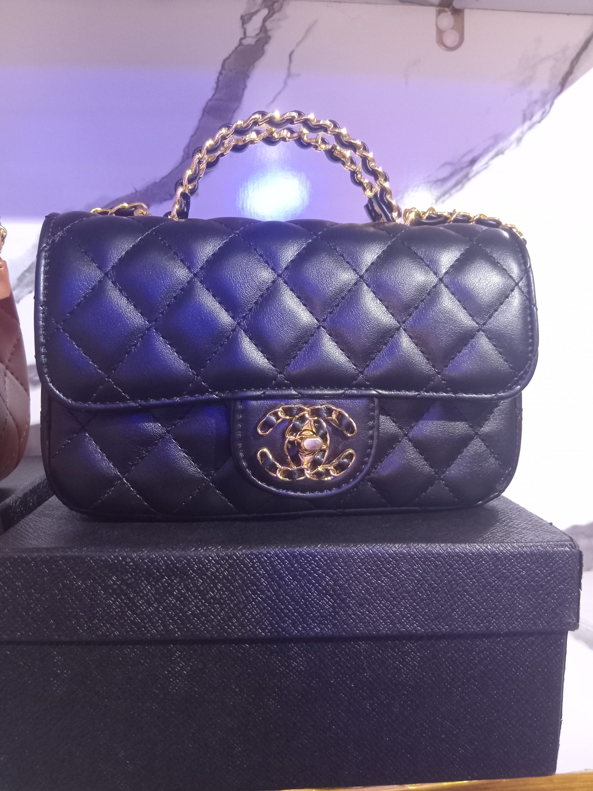 Quilted leather flap handbag with woven gold chain top handle and CC turn-lock closure shown in Black and Tan Brown.