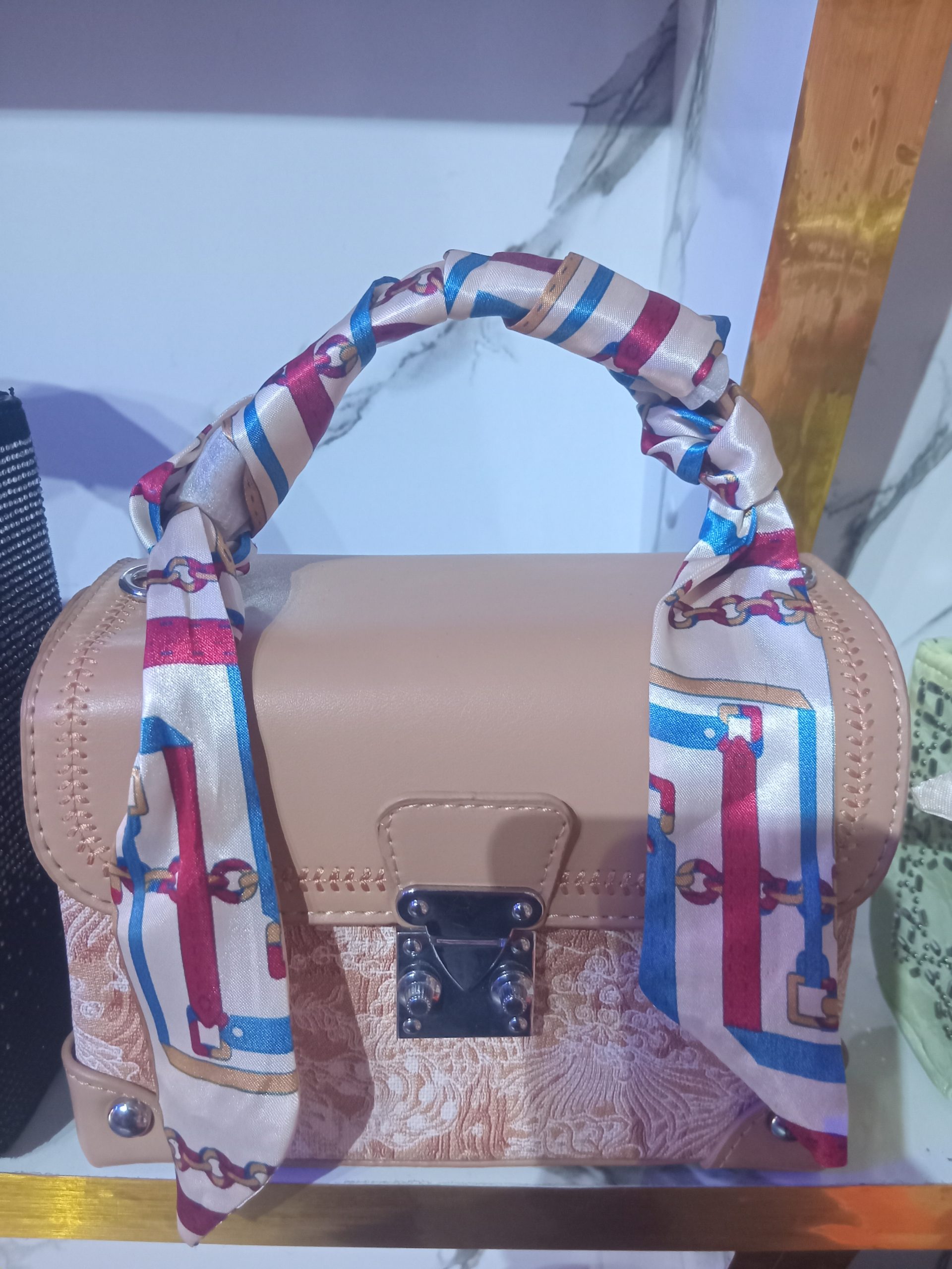 Louis Vuitton-inspired beige brocade trunk handbag with silver S-lock closure and printed scarf wrapped around top handle.