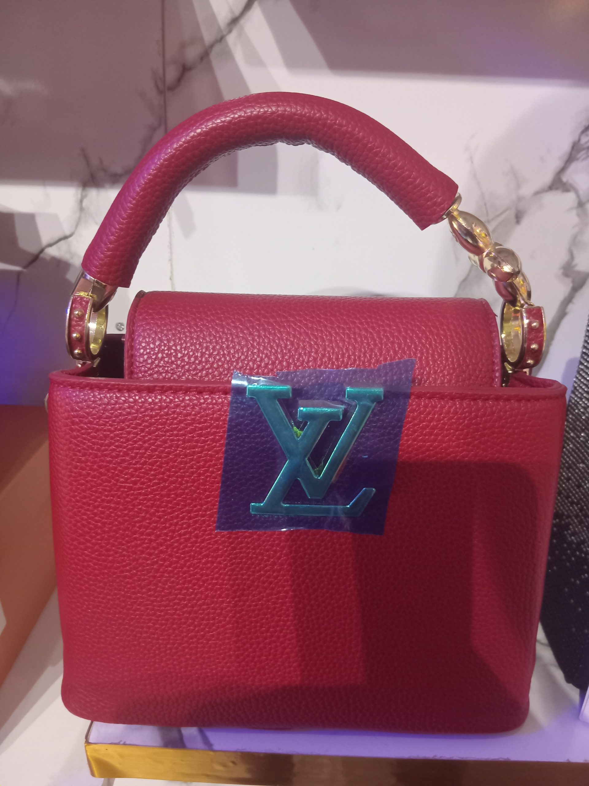 Red Louis Vuitton-inspired Capucines pebbled leather handbag with metallic LV initials logo and top handle.