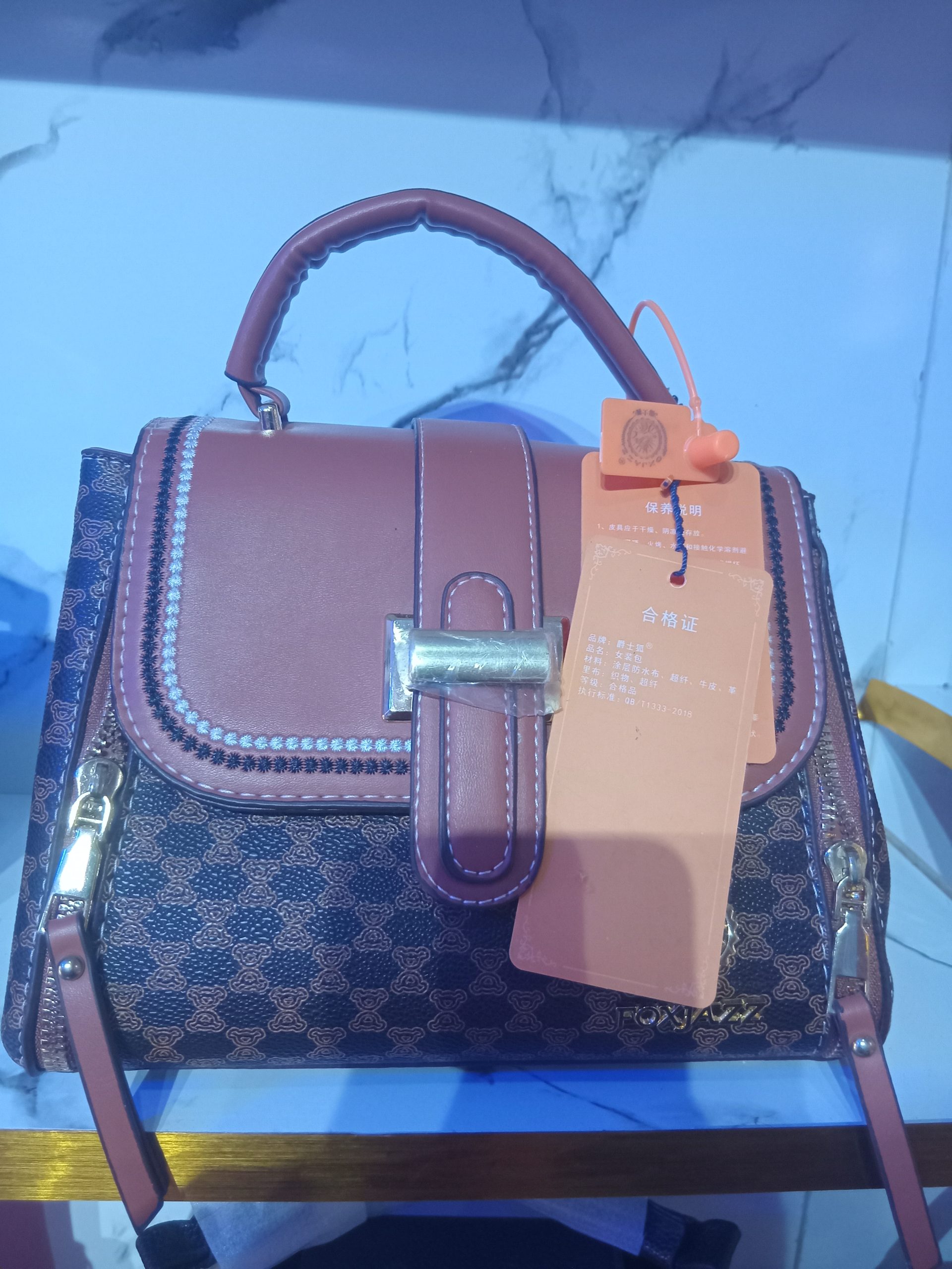 Brown monogram pattern satchel bag with smooth leather trim, contrast stitching along the flap, gold-tone hardware, and side zippers.