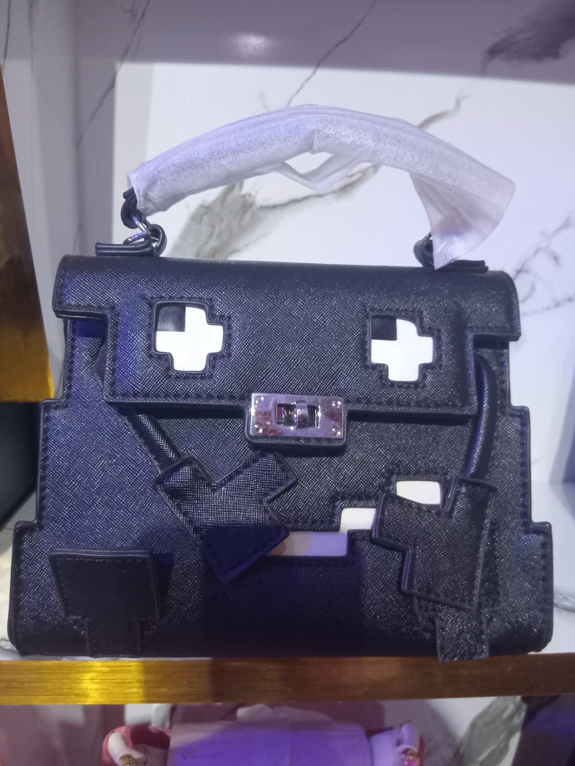 Black Saffiano leather pixelated Hermès Kelly style satchel bag with 8-bit cut-outs, white accents, and silver turn-lock hardware.