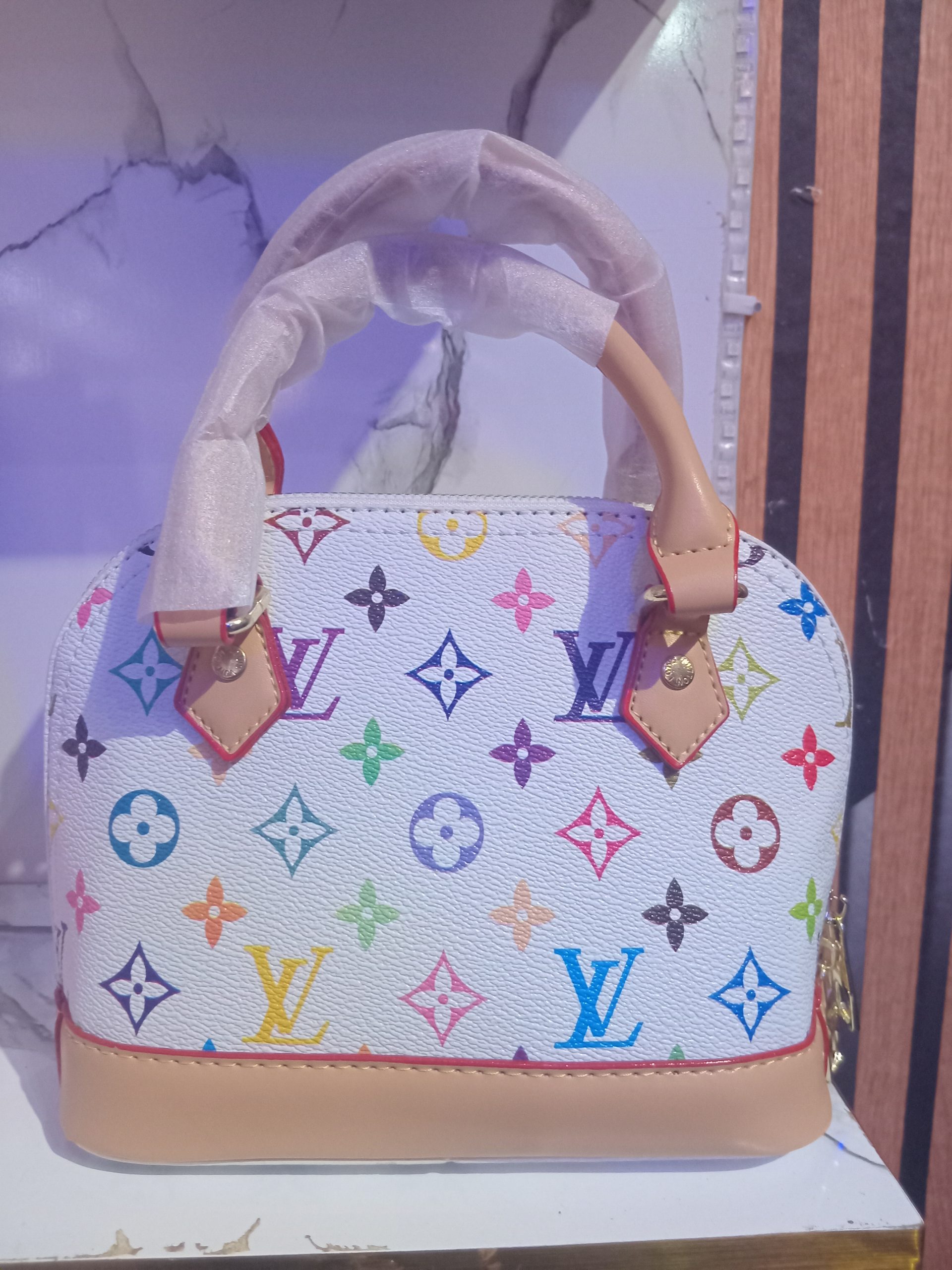 White Louis Vuitton-inspired Alma BB dome bag featuring a multicolour rainbow LV monogram print with tan leather trim and handles.