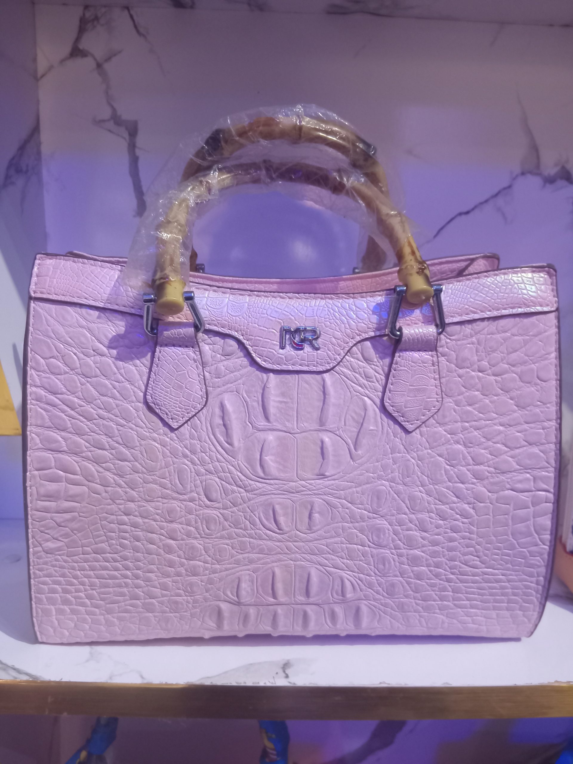 Light pink crocodile-embossed leather tote bag featuring natural curved bamboo top handles and silver hardware insignia.