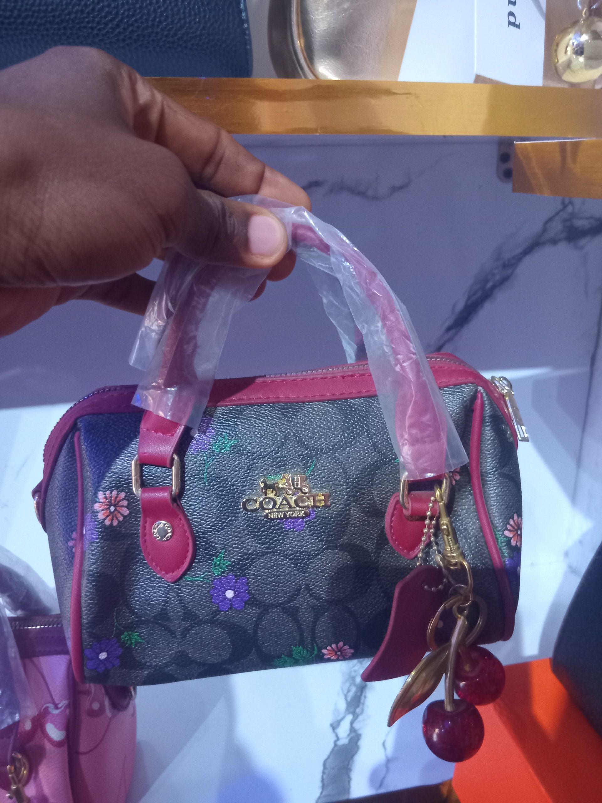 Coach-inspired signature monogram mini barrel satchel with floral print, magenta pink trim, gold-tone logo, and a hanging cherry charm.