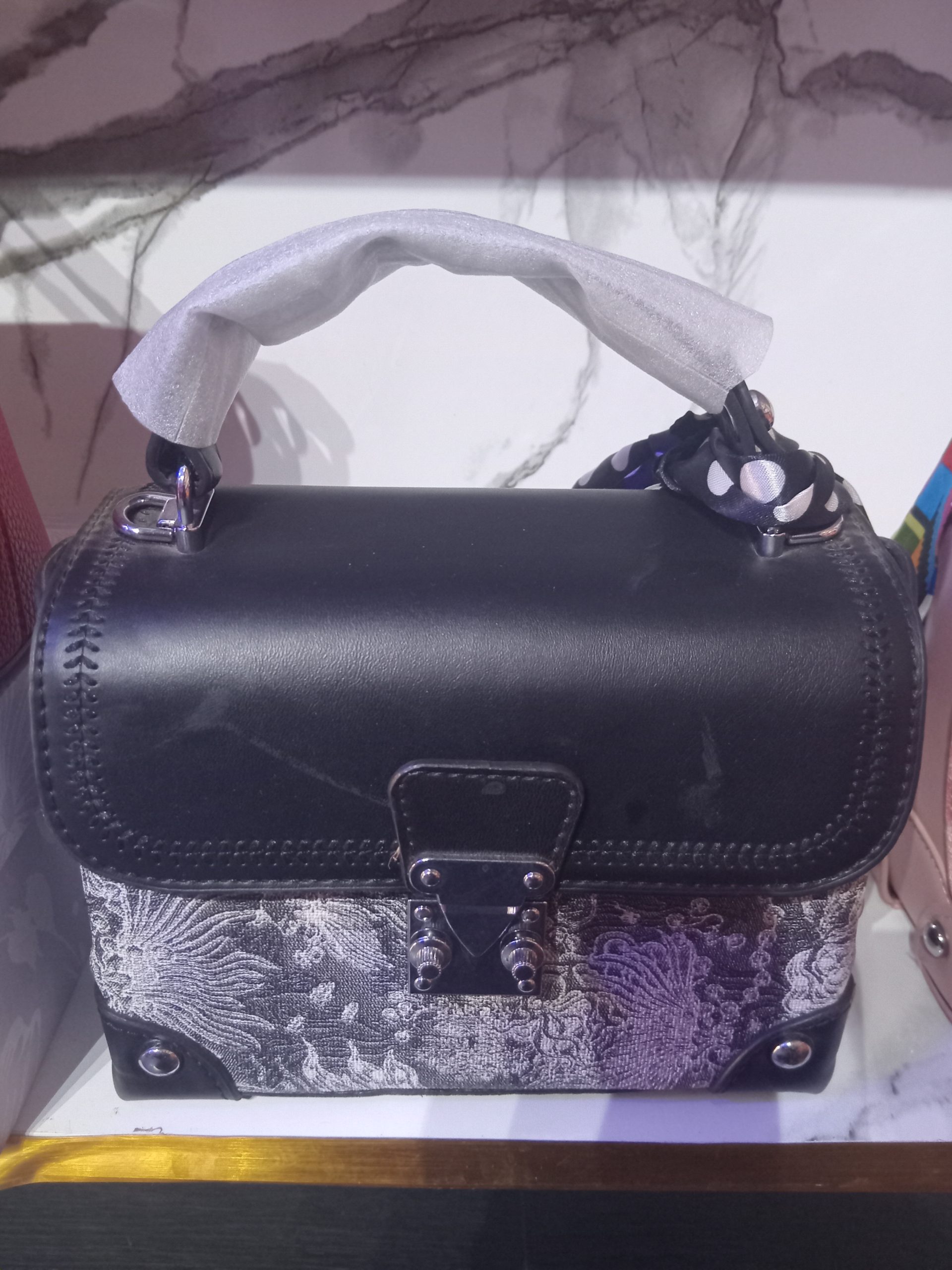 Louis Vuitton inspired brocade trunk handbag with scarf wrapped handle Black jacquard brocade mini trunk satchel featuring a black-and-white patterned lower body, smooth black flap, silver push-lock, and a wrapped top handle with a polka dot scarf.