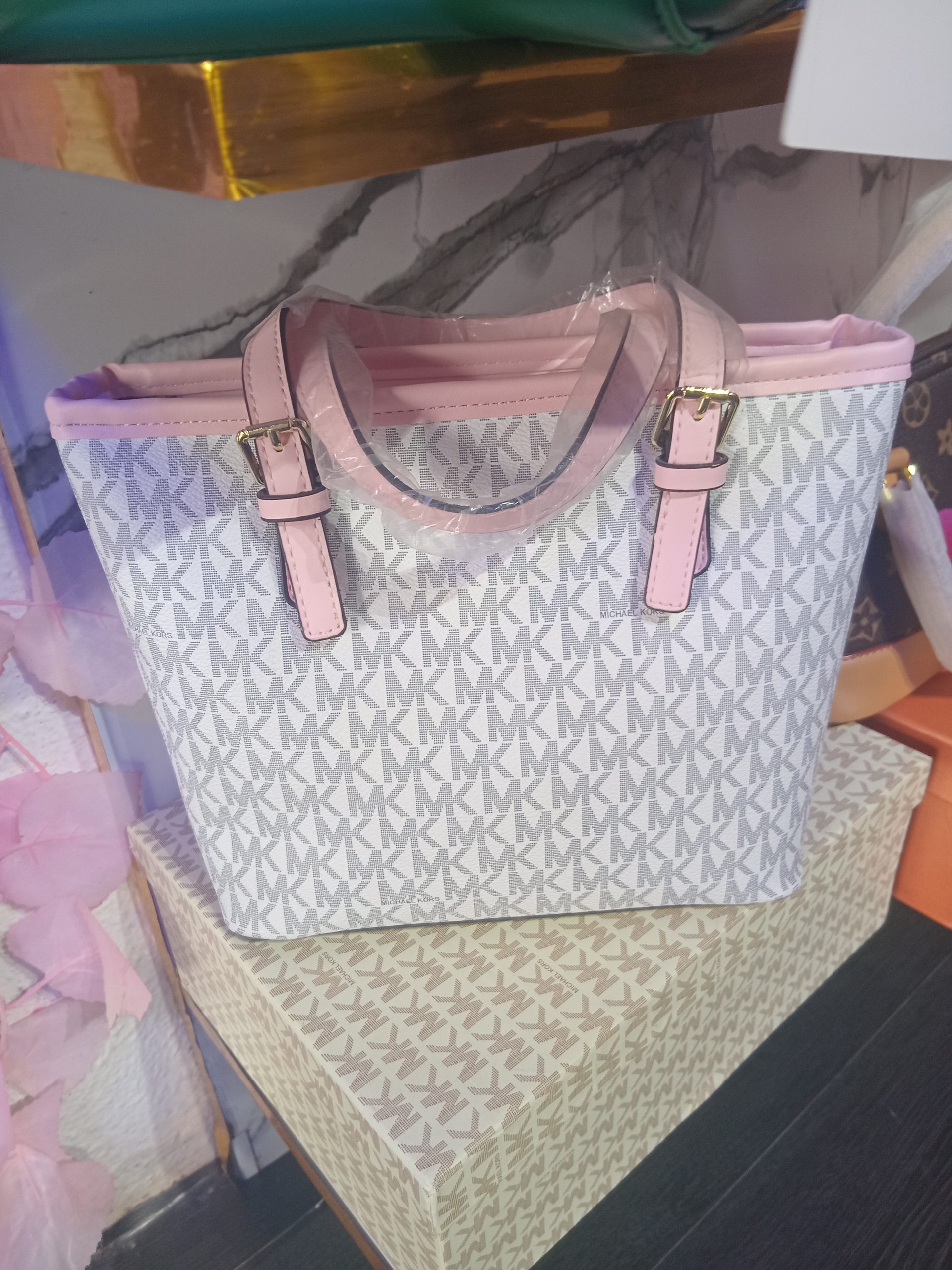 Michael Kors-inspired white and grey monogram print shopper tote bag featuring pastel pink trim, gold lettering, and hanging MK logo charm.