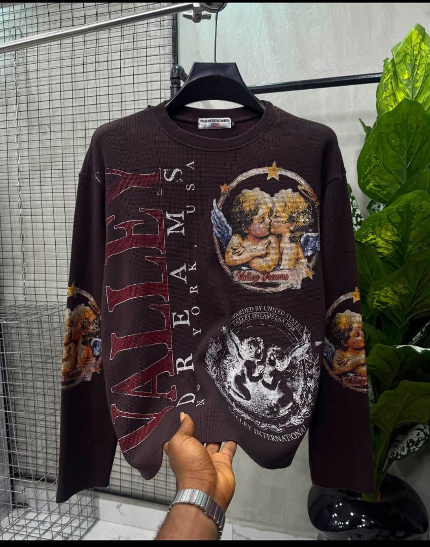 Dark brown graphic long-sleeve thermal top with angel artwork and "Valley Dreams" text hanging on a rack.