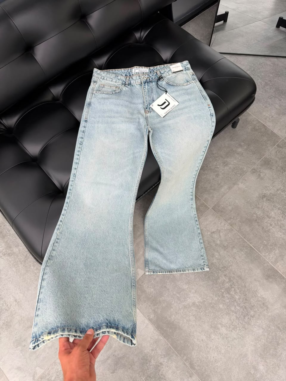 Light blue flare denim trousers laid flat on a dark leather couch.